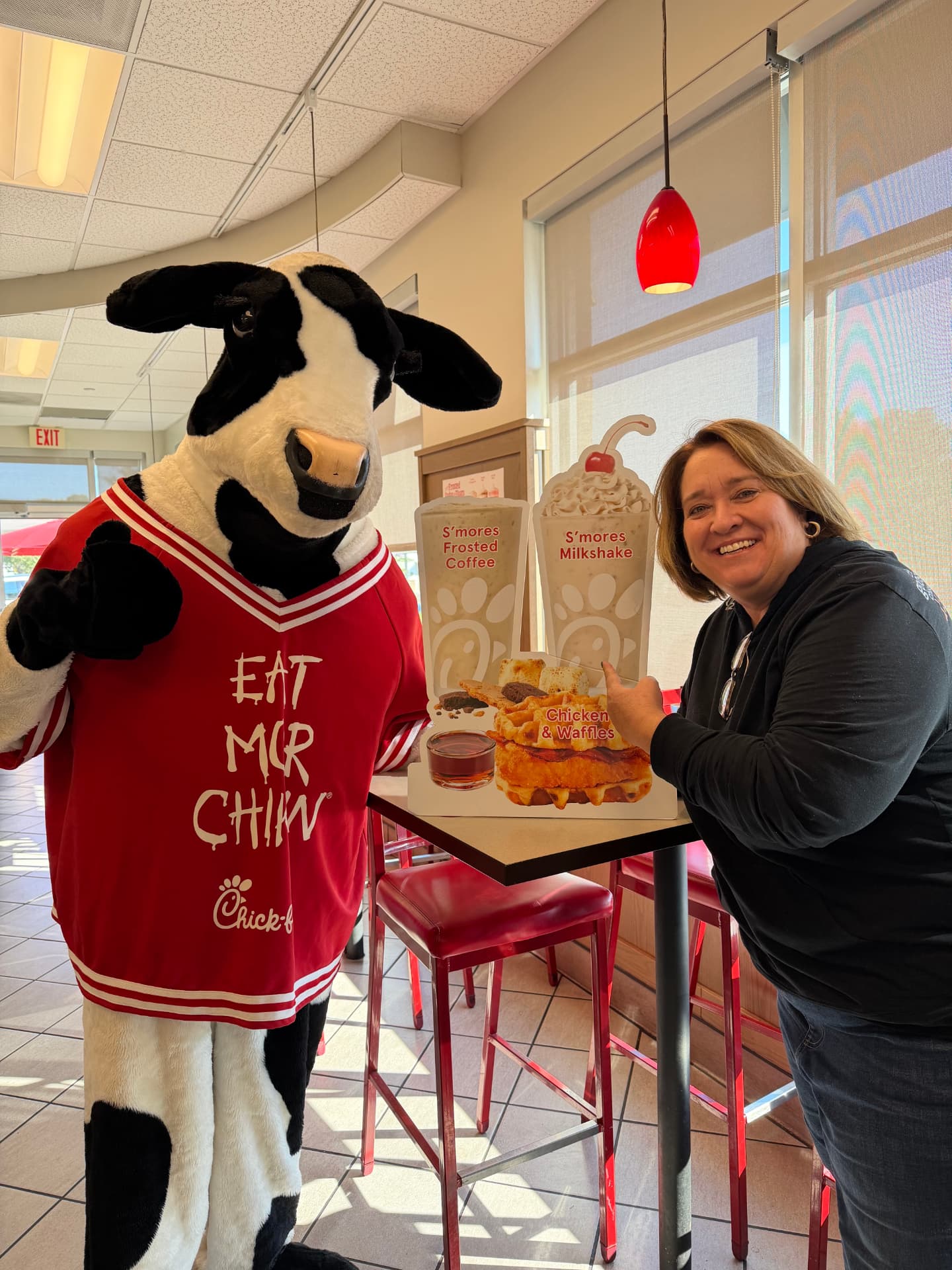 The Chick-fil-A cow mascot beside a runner pointing at the S'mores Milkshake display