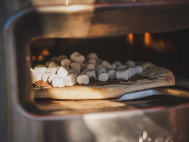 Marshmallows toasting over chocolate on a s'mores pizza in the wood-fired oven