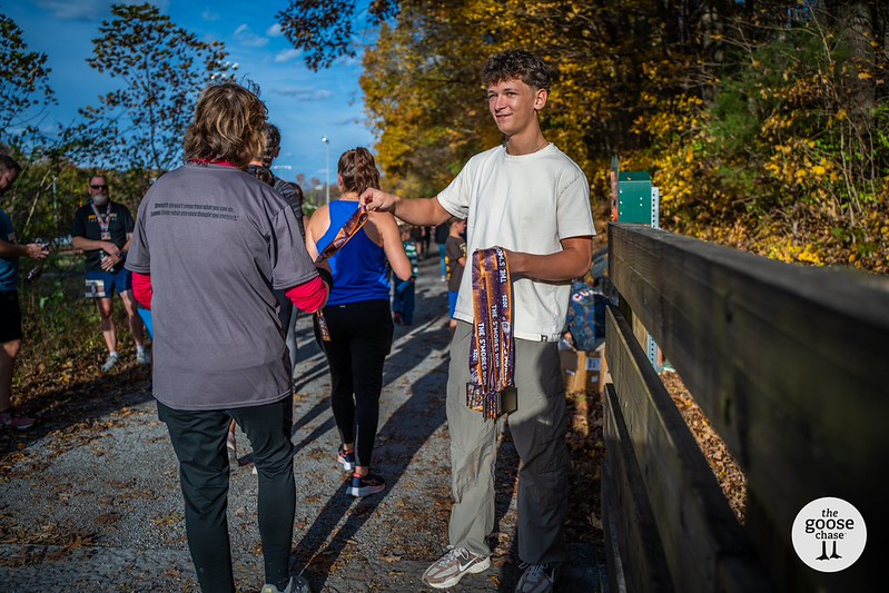 A volunteer hands a runner their S'mores Run medal at the finish