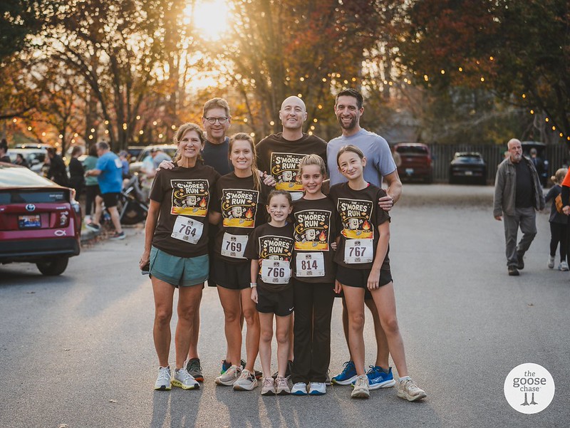 A family wearing race bibs gathers on the Townsend road at The S'mores Run, with The Goose Chase watermark visible
