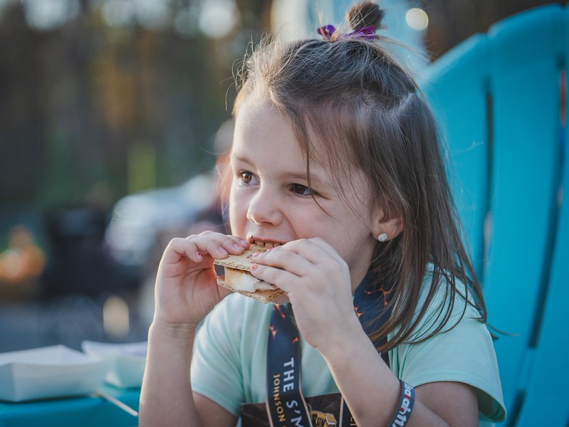 A young runner in her S'mores Run lanyard takes a big bite of a fresh s'more