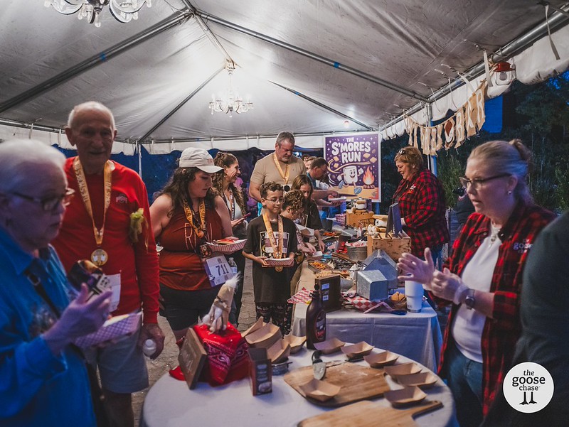 Participants gather around the s'mores table under the Townsend celebration tent, with The Goose Chase watermark visible