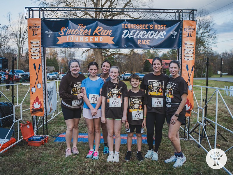A group of Townsend finishers with medals beneath the S'mores Run finish banner, with The Goose Chase watermark visible